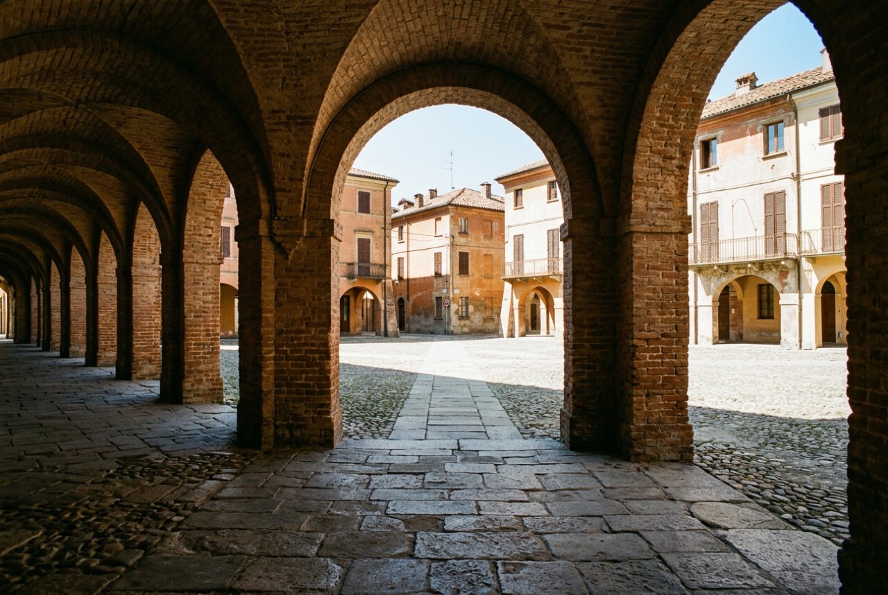 A colonnade of brick arches along a northern Italian street opening onto a sunlit square, warm shade, worn paving