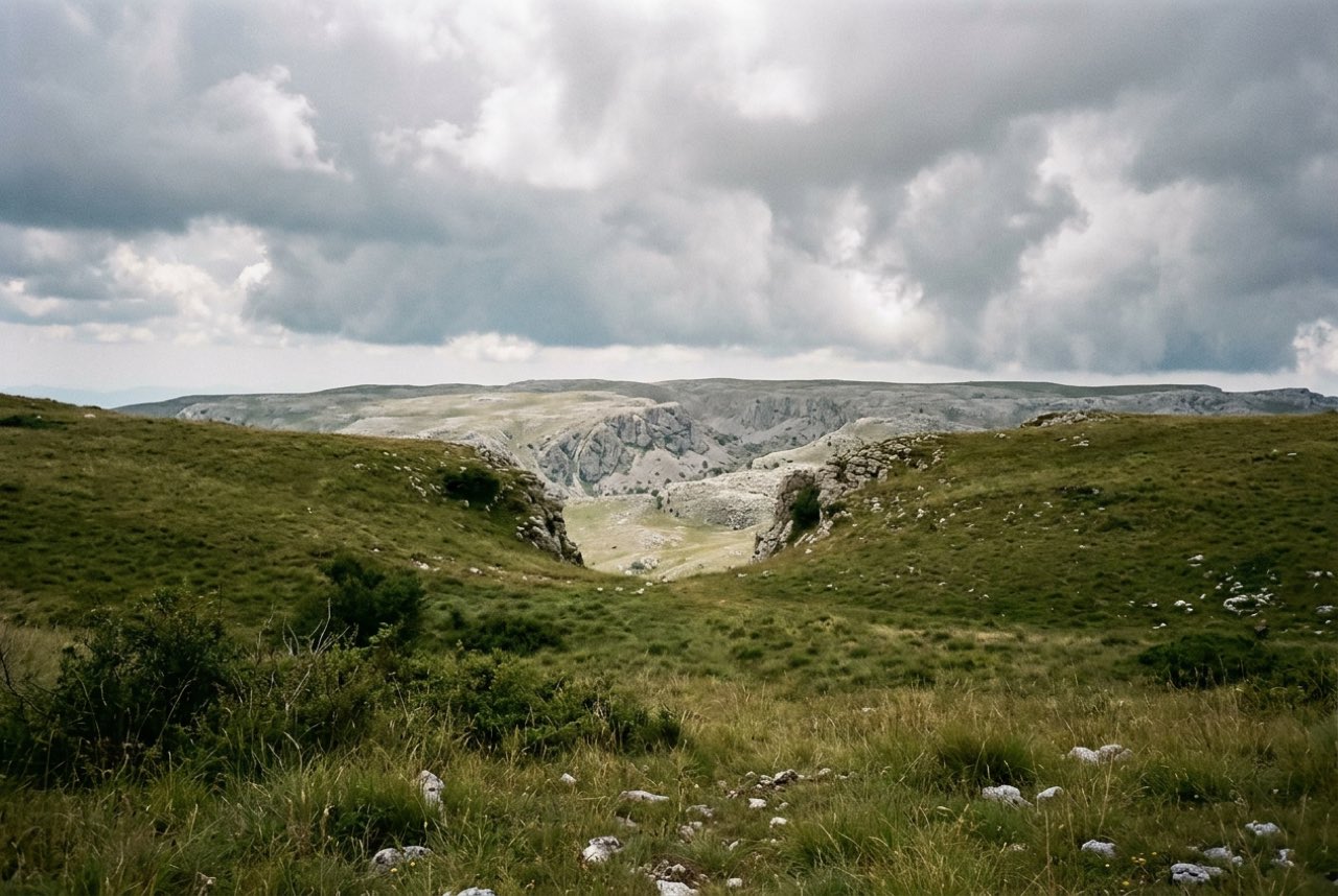 A col in an Apennine grass ridge opening onto a bare limestone plateau, storm light building